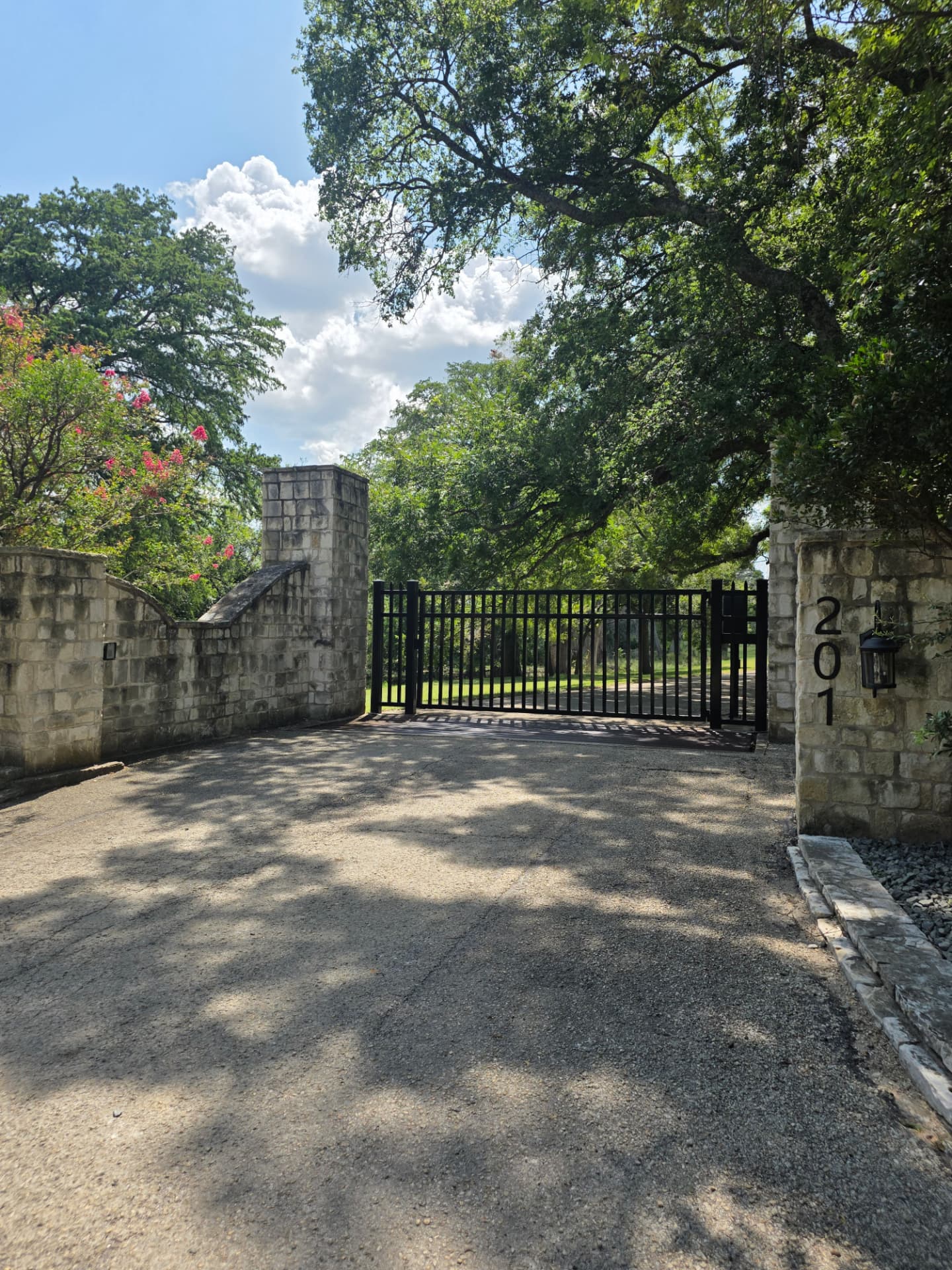 The limestone-and-iron entrance gate at Sussex Ranch in Comfort, Texas, shaded by live oaks