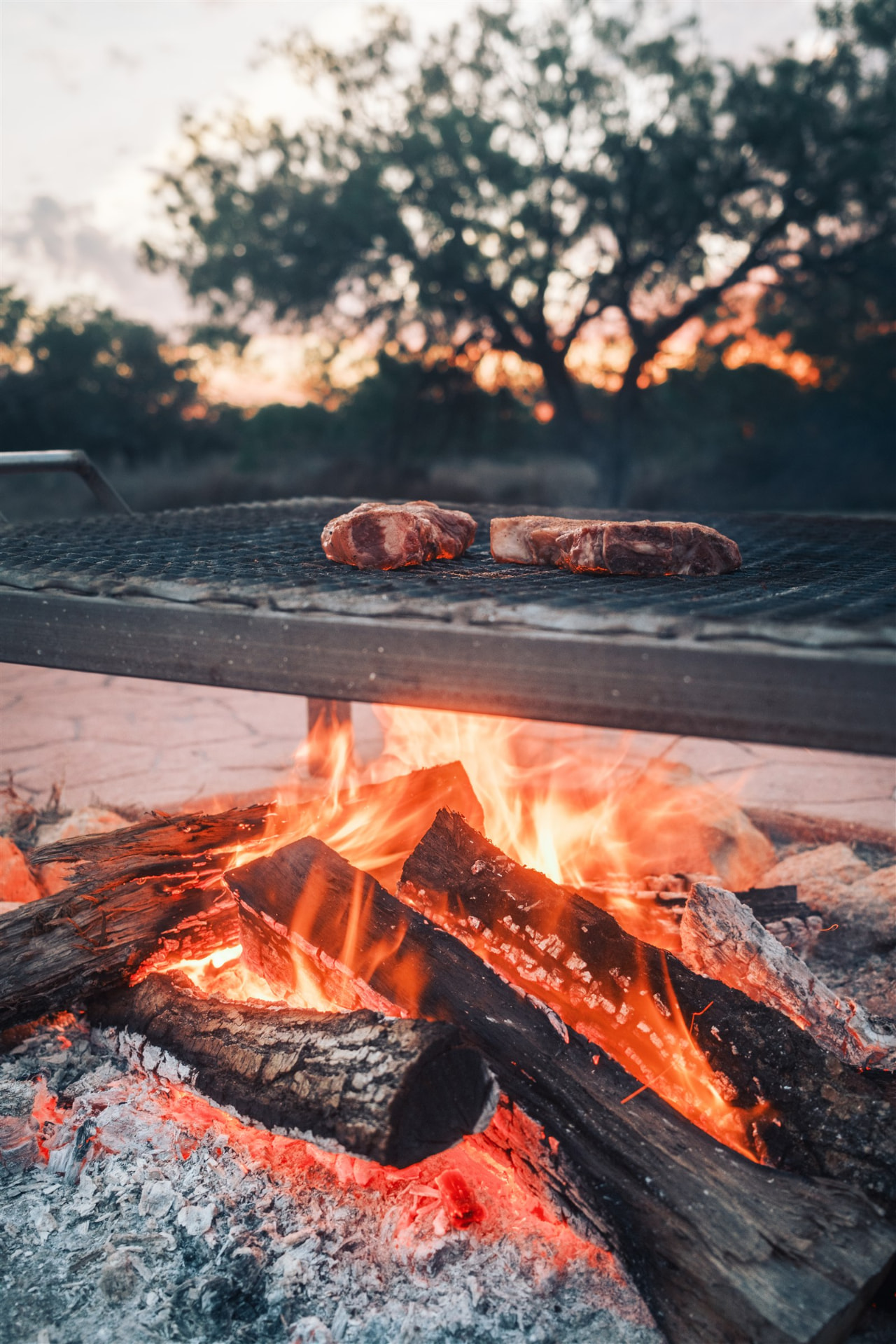 Sussex Ranch steaks grilling over an open wood fire, flames rising around the grate