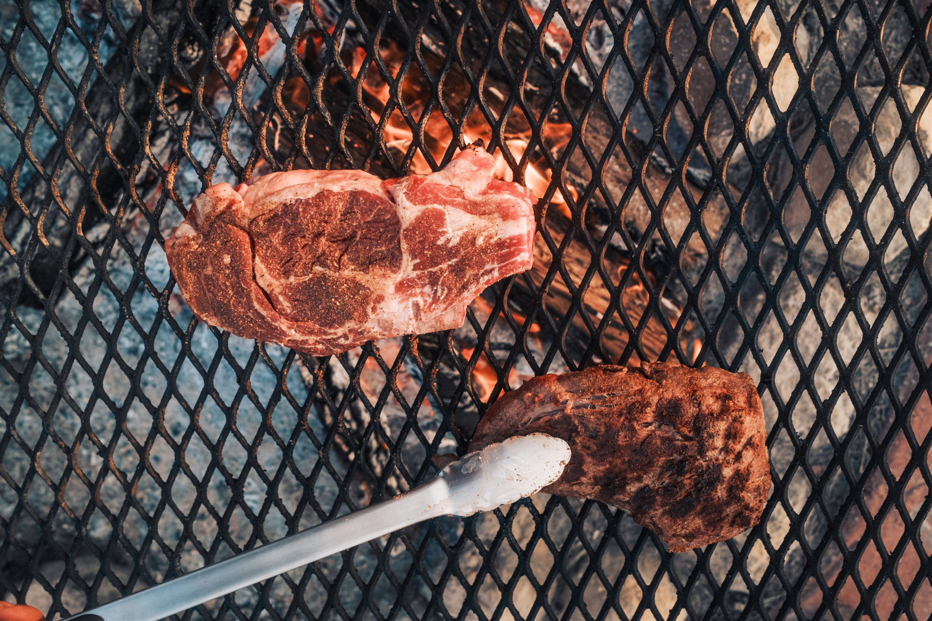 Close-up of a thick-cut Sussex Ranch steak searing on a hot grill grate over glowing coals